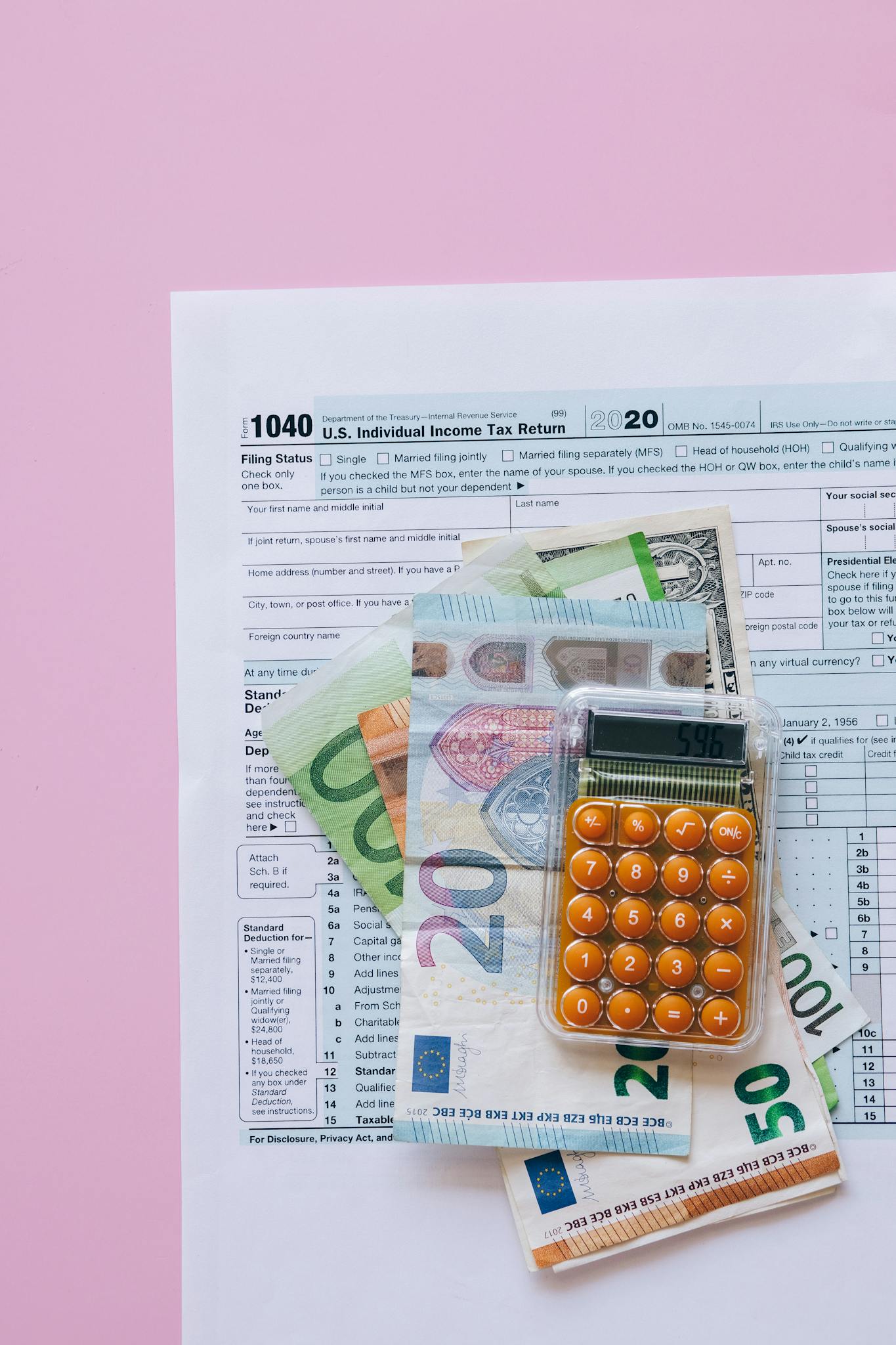 A vibrant flat lay of a calculator, euro banknotes, and US tax forms on a pink background.