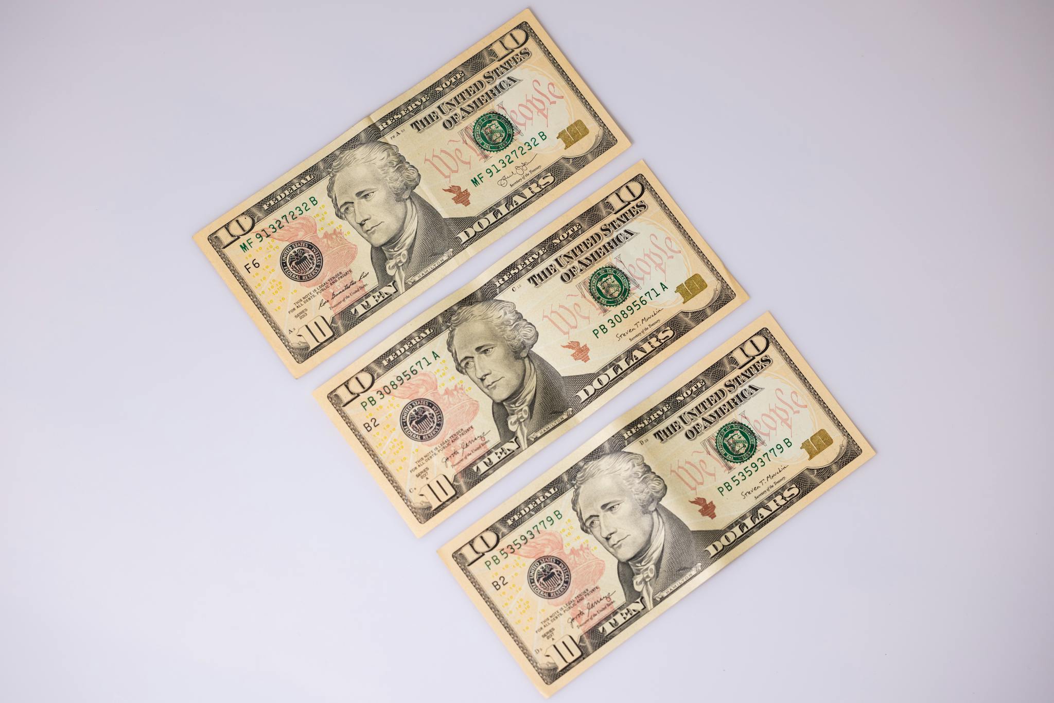 Close-up of three ten-dollar bills laid on a white surface, highlighting currency details.